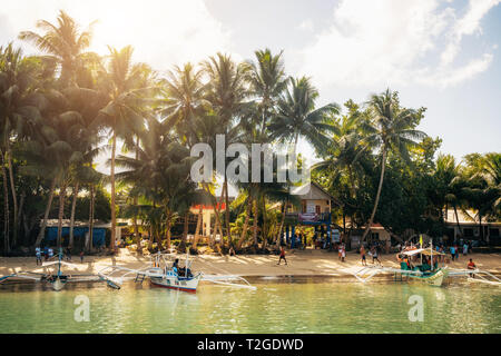 Port Barton, Palawan, Philippinen - Februar 4, 2019: Menschen auf tropischen Strand mit Bäumen. Traditionelle Boote im Wasser Stockfoto