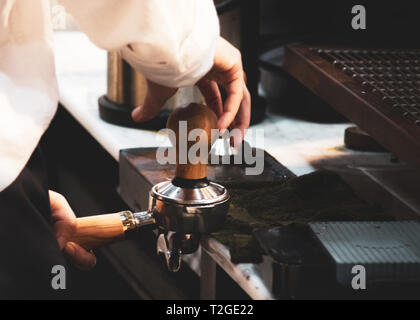 Barista in einem Café arbeitet, in der Nähe von barista Pressen gemahlenen Kaffee mit Sabotage, Barista, Kaffee Portafilter Konzept Stockfoto