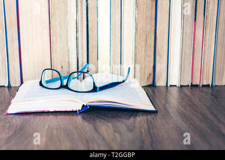 Gebundene Bücher auf weissem Holztisch, offenes Buch und Brille, kopieren Platz für Text Stockfoto