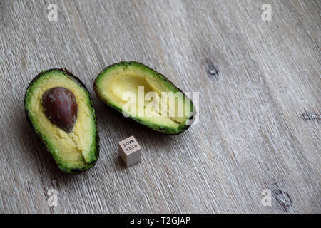 Konzept der liebevollen Avocados mit einem Schnitt avocado auf hölzernen Hintergrund mit einem holzschild mit der Nachricht Liebe Diese auf ihn Stockfoto