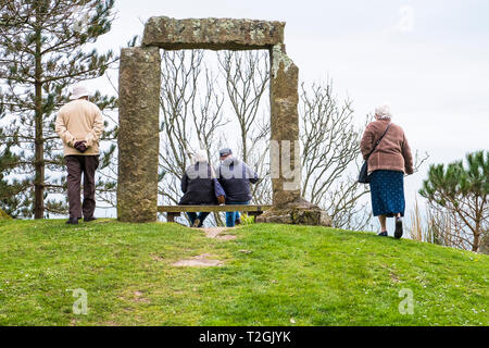 Besucher sitzen auf einer Bank unter einem monolithischen Arch einen viktorianischen Torheit errichtet in Gyllyngdune Gärten in Falmouth in Cornwall. Stockfoto