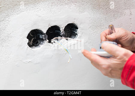 Elektriker Hand, die elektrischen Kabel, elektrische Steckdose an der Wand - Sanierung, im Bau, in der neuen Wohnung Stockfoto