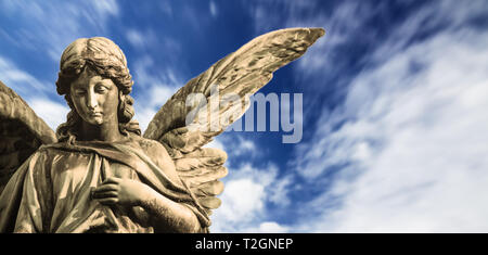 Schutzengel Skulptur mit offenen langen Flügel isoliert mit unscharfen weiße Wolken blauer Himmel. Engel traurigen Gesichtsausdruck Skulptur mit Augen zu und durch Hand in f Stockfoto