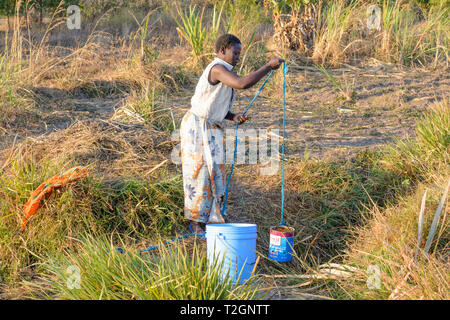 Malawische Frau zieht Wasser aus gut seicht in einem Dorf mit einer Farbdose und Seil Stockfoto