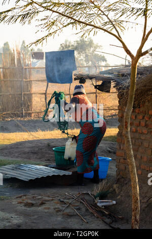 Malawische Frau zieht Wasser aus flachen gut mit einem Kunststoffbehälter Stockfoto