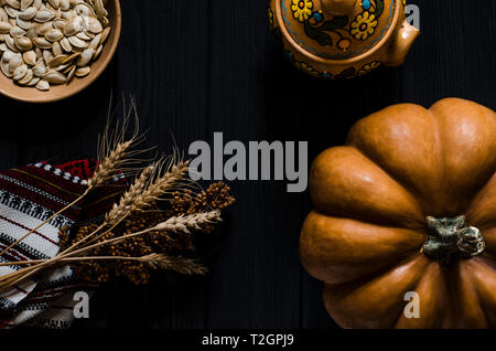 Orange Kürbis, Kürbis Samen und Weizenähren auf einem schwarzen Hintergrund Holz liegen. top View Stockfoto