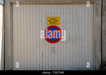 Weiß altes Garagentor mit einem verkehrsschild Parken verbieten und die Inschrift Ausfahrt Tag und Nacht kostenlos Stockfoto