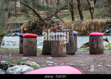 Tisch und Stühle von Baum Protokolle, mit bunten Kissen auf jedem log/Stuhl, in der Nähe eines Flusses. Konzept für Picknicks, Essen im Freien in der Natur. Stockfoto