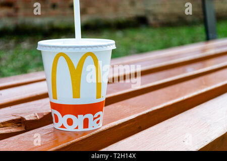 Sibiu, Rumänien - 26. März 2019: McDonalds Cup auf einer Parkbank aufgegeben, mit dem Deckel auf einem weißen Stroh und. Stockfoto