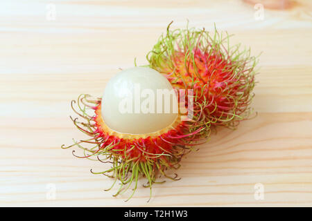 Ganze Früchte, frische reife Rambutan und geschält, zu zeigen Seinen weißen saftige Fruchtfleisch isoliert auf hölzernen Tisch Stockfoto