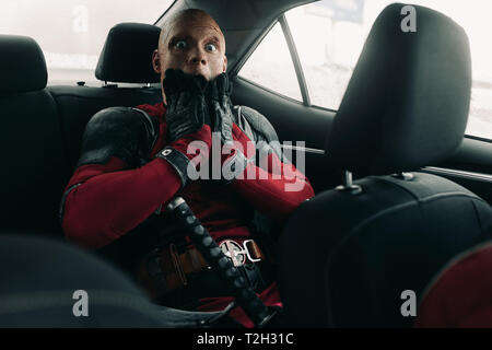 DNIPRO, UKRAINE - 28. MÄRZ 2019: Deadpool cosplayer im Auto mit der Waffe in der Hand posieren. Stockfoto