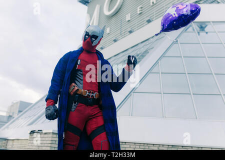 DNIPRO, UKRAINE - 28. MÄRZ 2019: Deadpool cosplayer mit Ballon in der Hand vor dem Hintergrund der urbanen Landschaft posieren. Stockfoto