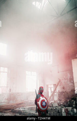 DNIPRO, UKRAINE - 28. MÄRZ 2019: Deadpool cosplayer im Innenbereich mit Waffe und Schild posiert auf dem Hintergrund von Rauch. Stockfoto
