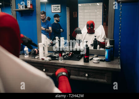 DNIPRO, UKRAINE - 28. MÄRZ 2019: Deadpool Cosplayer posiert und sitzt auf einem Sessel im barbershop. Stockfoto