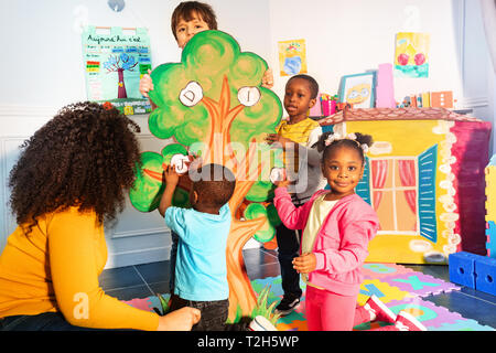 Kleine Kinder im Kindergarten Buchstaben auf den Baum wie Entwicklung Spiel mit Lehrer Stockfoto