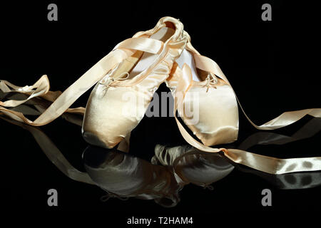 Ein paar Ballett Schuhe, dekorativ auf einem schwarzen Hintergrund angeordnet. Die Schuhe sind im Hintergrund reflektiert. Stockfoto