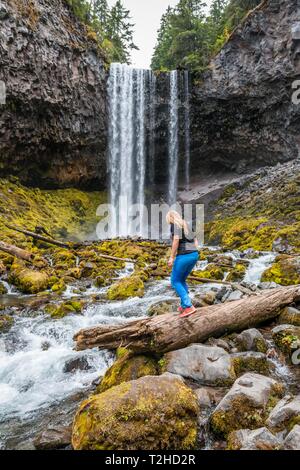 Junge Frau durchquert Fluss, Wanderer, Wasserfall fließt über Felsvorsprung, Tamanawas fällt, wilden Fluss Cold Spring Creek, Oregon, USA Stockfoto