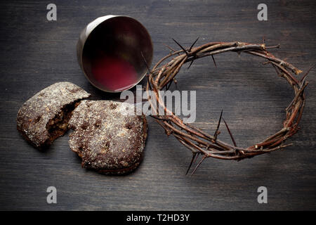 Gemeinschaft und Leidenschaft - ungesäuertes Brot Kelch Wein und Dornenkrone auf hölzernen Tisch Stockfoto