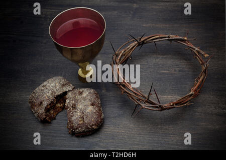 Gemeinschaft und Leidenschaft - ungesäuertes Brot Kelch Wein und Dornenkrone auf hölzernen Tisch Stockfoto