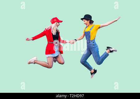 Volle Beine Körper größe Portrait von zwei glückliche Schreien stilvolle hipster Mädchen in modische Kleidung springen in die Luft und feierte einen Gewinn. Pflege Stockfoto