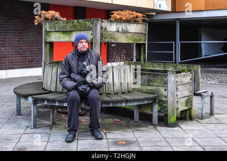 Älterer Mann mit Kamera beruht auf einer Bank in Moabit, Berlin. Rustikale Holzbank mit Blumentöpfe Stockfoto