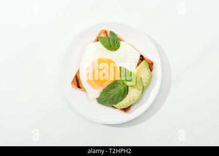 Blick von oben auf Toast mit Spiegelei und schneiden Avocado auf Platte auf weiße Oberfläche Stockfoto