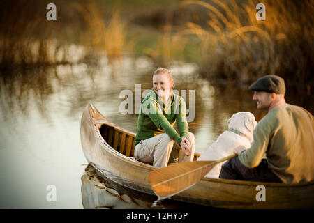 Junge erwachsene Paare mit Hund Rudern an einem See in einem Kanu bei Sonnenuntergang. Stockfoto