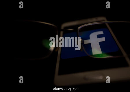 Facebook Logo auf einem Smartphone Display angezeigt wird, ist der Schwerpunkt der Blick durch die Augen Brille Stockfoto
