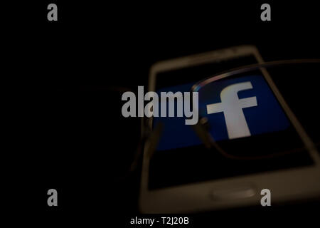 Facebook Logo auf einem Smartphone Display angezeigt wird, ist der Schwerpunkt der Blick durch die Augen Brille Stockfoto