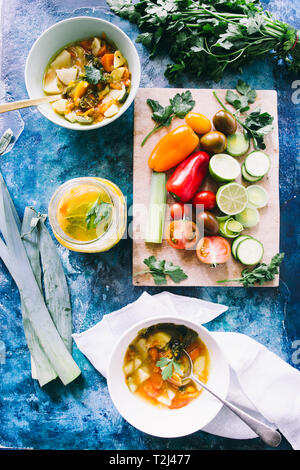 Minestrone, auf die Schüssel und der Mixbecher mit Gemüse schneiden auf einem cutboard Kirschtomate Braun, Kalk, und Lauch runde Stücke Stockfoto