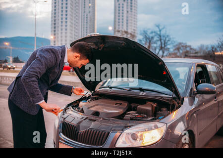 Einen müden Arbeiter steht neben seinem Auto formell gekleidet und Suchen über die Autos Motor Problem besorgt. Stockfoto