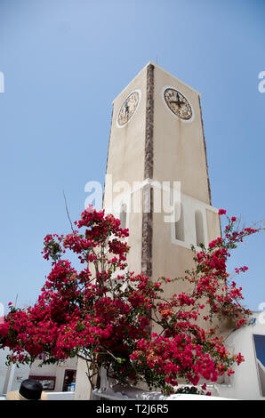 Ein Uhrenturm auf Santorini, umgeben von wunderschönen, magentafarbenen Bougainvillea. Stockfoto