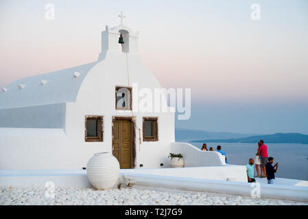 Eine weiße Kykladen home sitzt an der felsigen Küste von Santorini, mit Blick auf das Ägäische Meer bei Sonnenuntergang. Stockfoto
