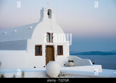 Eine weiße Kykladen home sitzt an der felsigen Küste von Santorini, mit Blick auf das Ägäische Meer bei Sonnenuntergang. Stockfoto