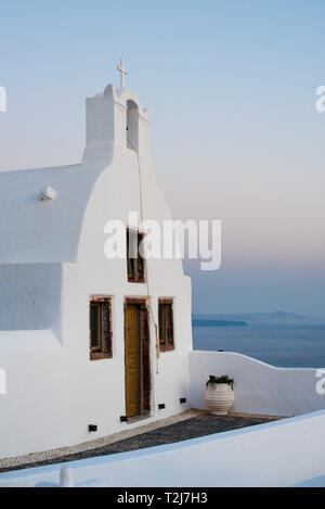 Eine weiße Kykladen home sitzt an der felsigen Küste von Santorini, mit Blick auf das Ägäische Meer bei Sonnenuntergang. Stockfoto
