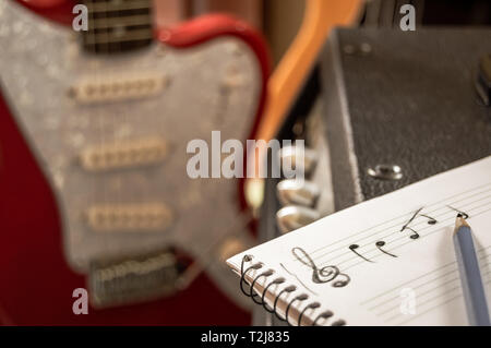 Komponieren von Musik in einem Personal Notebook mit Gitarre und Bass im Hintergrund. Musiker schreiben im Music Studio. Komponieren im Violinschlüssel. Stockfoto