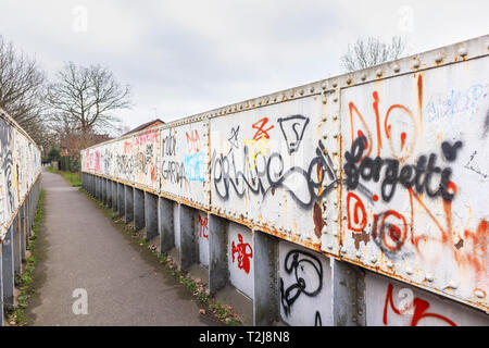 Sprühfarbe grafitti auf ein altes rostiges Eisen bahn Brücke auf einem Fußweg in Woking, Surrey, England, Großbritannien Stockfoto