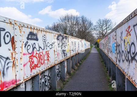 Sprühfarbe grafitti auf ein altes rostiges Eisen bahn Brücke auf einem Fußweg in Woking, Surrey, England, Großbritannien Stockfoto