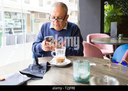 Stattliche mittleren Alters ältere Menschen trinken Kaffee im Restaurante und lächelt glücklich Genießen und entspannen Sie ihr Smartphone in den Ruhestand Stockfoto