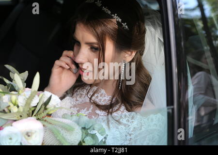 Hochzeit Foto von der Braut die im Auto sitzt, mit einem Blumenstrauß und am Telefon zu sprechen. Stockfoto