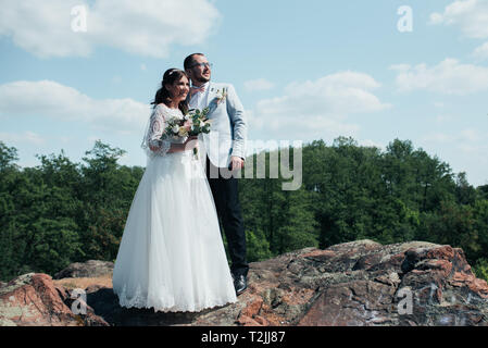 Hochzeit Foto eines bärtigen Bräutigam mit Brille in einer grauen Jacke und eine Braut, die sich auf einem Felsen. Stockfoto