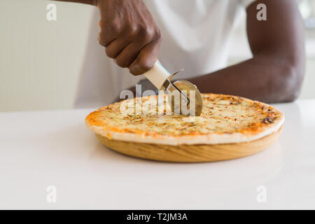 Nahaufnahme der afrikanischen Mann schneidet ein Stück Käse Pizza mit einem Cutter Stockfoto