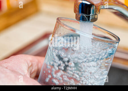 Closeup Aufnahme eines Mannes, gießen ein Glas frisches Wasser aus einer Küche Wasserhahn