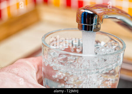 Closeup Aufnahme eines Mannes, gießen ein Glas frisches Wasser aus einer Küche Wasserhahn Stockfoto