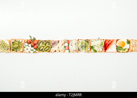 Blick von oben auf die Toasts mit geschnittenem Obst, Gemüse und Erdnüsse auf Weiß Stockfoto