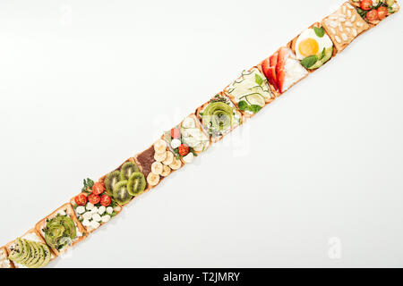 Blick von oben auf die Toasts mit geschnittenem Obst, Gemüse und Erdnüsse auf Weiß Stockfoto