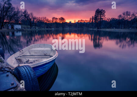 Sonnenuntergang Szene in einem Park in Bukarest mit einem Boot im Vordergrund zum Ufer und dramatische Wolken im Himmel geschossen gebunden zu Beginn des autolöscher Stockfoto