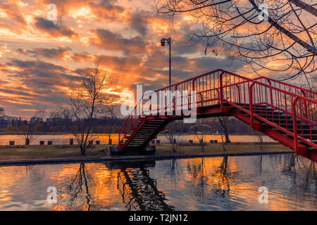 Sonnenuntergang von einem Park in Bukarest mit Sonnenstrahlen, die sich aus den Wolken und ein rote Metall Brücke im Vordergrund Schuß zu Beginn des Sp gesehen Stockfoto