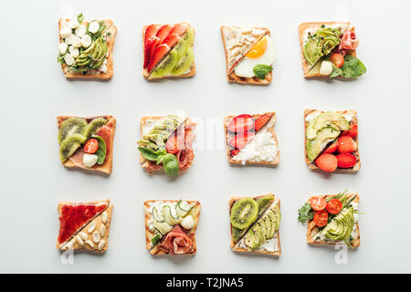 Blick von oben auf die leckeren Toast mit Obst, Gemüse und Basilikum isoliert auf weißem Stockfoto