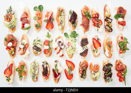 Hintergrund der köstliche italienische Bruschetta mit Lachs, Schinken, getrocknete Tomaten, Avocado, Erdbeeren und Kräutern auf Weiß Stockfoto